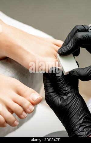 Mani di pedicurist che schiantano il toenail della donna da unghia bianca nel salone delle unghie Foto Stock