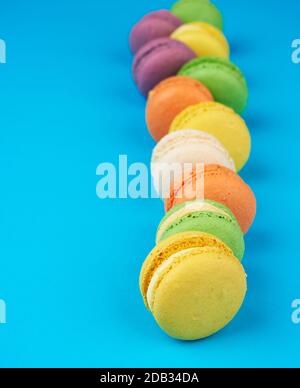 macaroni rotondi multicolore al forno con crema si trovano in una linea su uno sfondo blu, primo piano Foto Stock