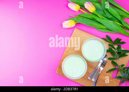 Yogurt al limone alla menta con kiwi in ciotole per insalata su tavola di legno insieme a tulipani su sfondo rosa. Foto Stock