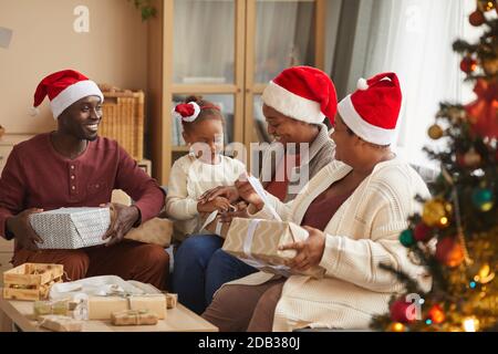 Ritratto di felice famiglia afroamericana che apre regali di Natale mentre indossa Cappelli di Santa e godersi la stagione delle vacanze a casa Foto Stock