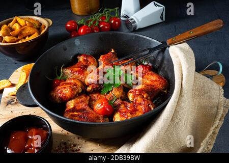 Ali di pollo speziate al miele con spicchi di patate Foto Stock