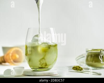 Tè Matcha latte ghiacciato con panna montata in bicchiere. Latte Matcha e ingredienti su sfondo bianco in marmo. Spazio di copia per txt o desi Foto Stock