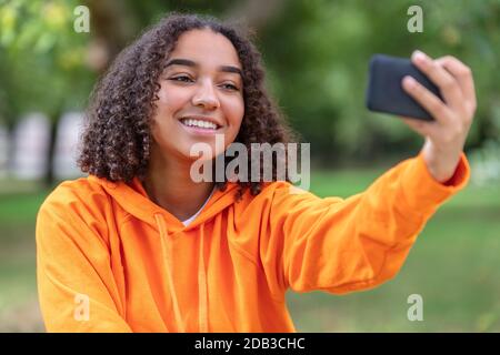 Bella felice mista razza Africana americana giovane donna adolescente femmina bambino sorridente con denti perfetti scattando foto selfie all'aperto con c Foto Stock