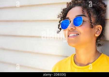 Ragazza adolescente cool teen misto razza biracial African American femmina giovane donna che indossa occhiali da sole blu e una t-shirt gialla vacanza sorridente Foto Stock