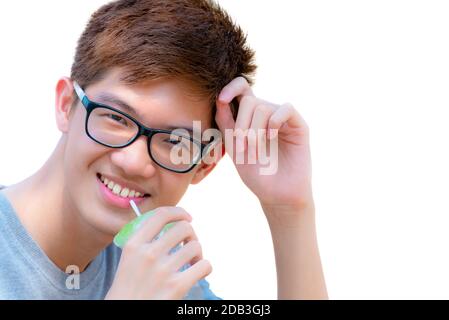 Primo piano faccia asiatico bel ragazzo adolescente che indossa bicchieri bere acqua da paglia in tazza di plastica, ritratto giovane hipster allegro uomo sorridente con Foto Stock