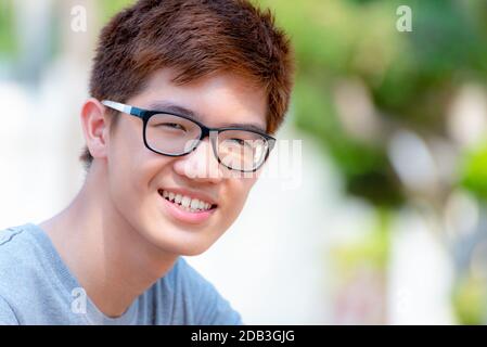 Primo piano faccia Asian bel ragazzo adolescente indossare occhiali, Ritratto allegro hippster giovane uomo sorridente con un volto felice al parco sulla natura verde bac Foto Stock