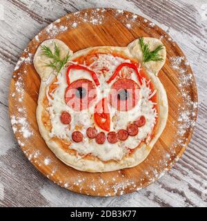 Pizza bambino sotto forma di faccia di un animale su un vassoio rotondo di legno Menu per bambini Foto Stock