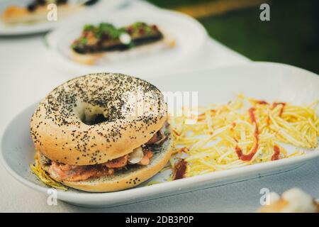 Piatto proposto in una festa gastronomica composta da un bagel con semi e farcito con frutti di mare con patatine di paglia Foto Stock