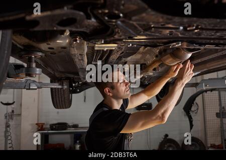 bel maschio caucasico che ripara il fondo dell'automobile, controlli ed esamini tutti i particolari. uomo duro in uniforme di lavoro Foto Stock