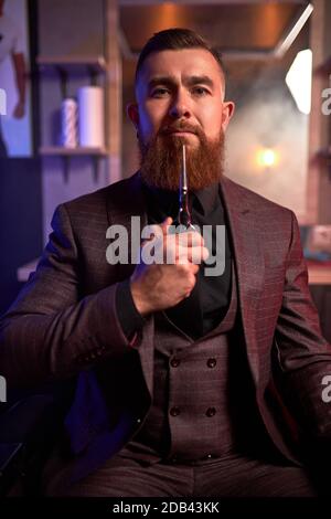 lo stylist professionale dei capelli è pronto per tagliare i vostri capelli o barba, maschio in abito sul posto di lavoro, in posa in stanza buia Foto Stock