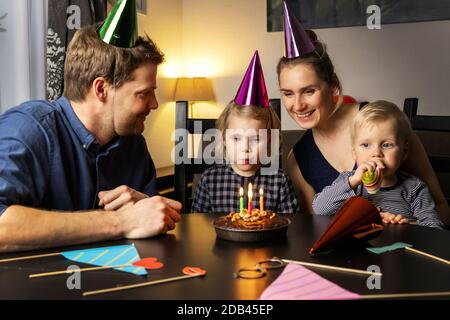 giovane famiglia felice che celebra il compleanno della figlia a casa. ragazza che soffia fuori le candele sulla sua torta Foto Stock