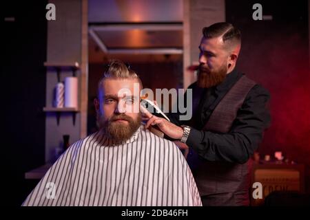 taglio capelli al parrucchiere, in salone. barbiere maschio tagli i capelli sulla testa del bel giovane cliente, il processo di creazione di acconciature per gli uomini da professionista Foto Stock