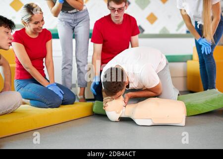 Classe CPR con giovani istruttori caucasici che parlano e dimostrano aiuto al primo soccorso, manichino cpr sul pavimento Foto Stock