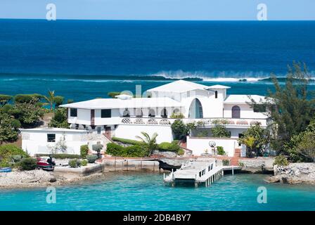 La casa residenziale di colore bianco costruita su una stretta striscia di terra sull'Isola del Paradiso tra il Porto di Nassau e il Mare dei Caraibi (Bahamas). Foto Stock