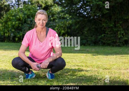 Ritratto esterno di una bella donna bionda di mezza età sorridente acqua potabile rilassante dopo esercizio fisico, corsa o stile di vita fitness Foto Stock