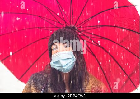 Ragazza graziosa allegra con protezione della maschera di faccia che tiene l'ombrello mentre Passeggiate fuori in città sotto la pioggia - concetto circa la donna cammina sulla th Foto Stock