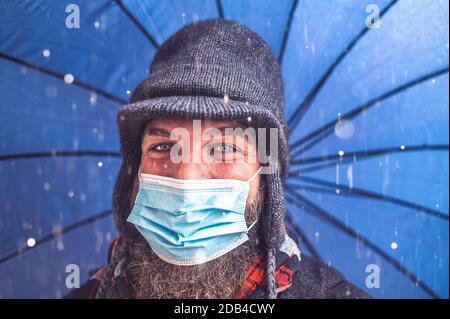 Uomo bearded con maschera di faccia che tiene l'ombrello e che fa un Selfie sotto la pioggia - concetto circa il ragazzo cammina sopra La strada in tempo di coronavirus - nuovo normale Foto Stock