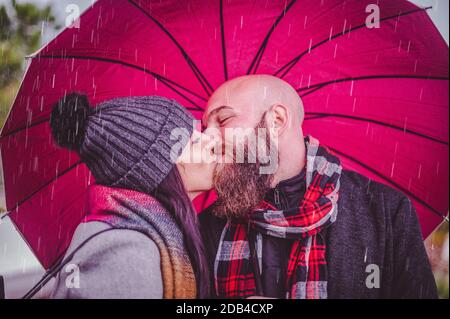 Giovane coppia felice bacio sotto un ombrello su una città street - primo piano ritratto di uomo bearded e bella donna - coppia amorosa sorridente sotto una u Foto Stock