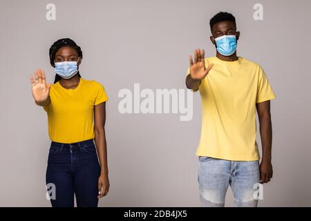 Assistenza sanitaria durante la quarantena e pandemia. Giovane coppia afroamericana indossando maschere mediche protettive per la protezione da virus su studio grigio b Foto Stock