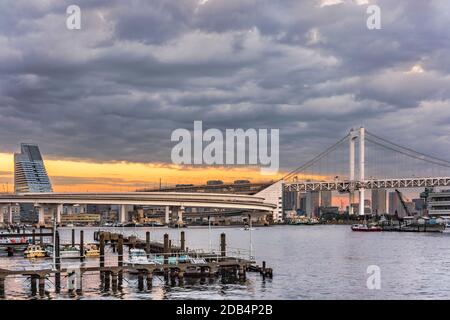 Autostrada circolare che conduce al Ponte dell'Arcobaleno con Cargo e navi da crociera ormeggiate o in barca a vela nella Baia di Odaiba a Tokyo. Foto Stock