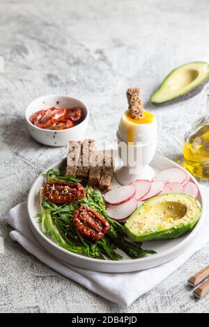 colazione nutriente: aglio selvatico, pomodori secchi, pane integrale, avocado, semi e uova bollite. buon concetto nutrizionale Foto Stock