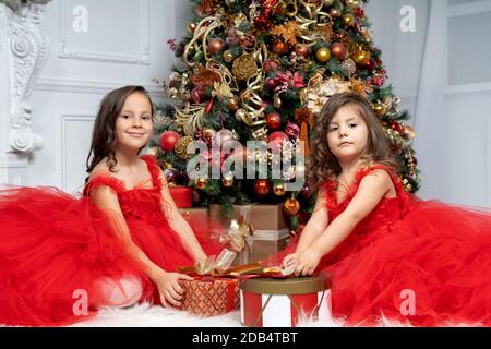 due ragazze belle piccole in abiti magnifici di fronte L'albero di Natale Foto Stock