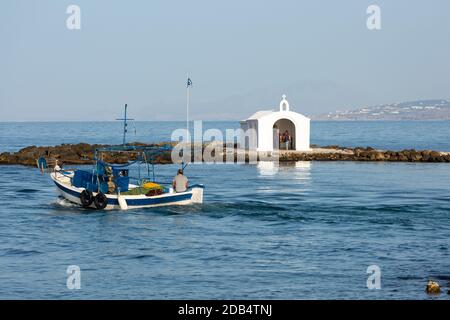 Una barca da pesca locale passa di fronte alla Cappella di Agios Nikolaos nel villaggio di Georgioupoli, Creta, Grecia Foto Stock