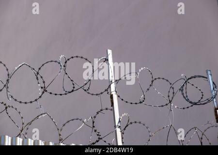 Da sotto recinzione di metallo con filo spinato sulla parte superiore localizzato contro il muro grigio sulla strada Foto Stock