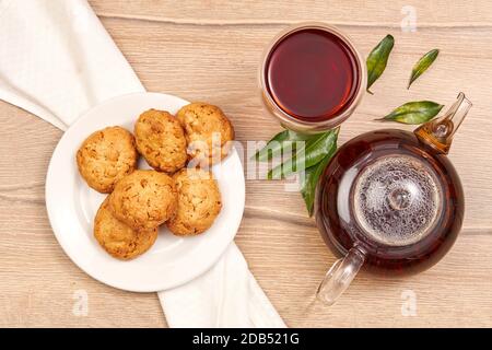 Teiera con set di tè caldo, tazza di tè e biscotti piccoli su un tavolo di legno Foto Stock