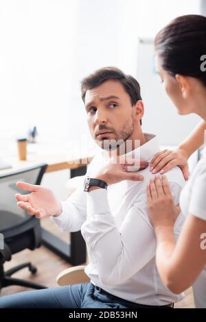 Massaggiatrice massaggiante spalla di uomo d'affari gesturing in ufficio su sfondo sfocato Foto Stock