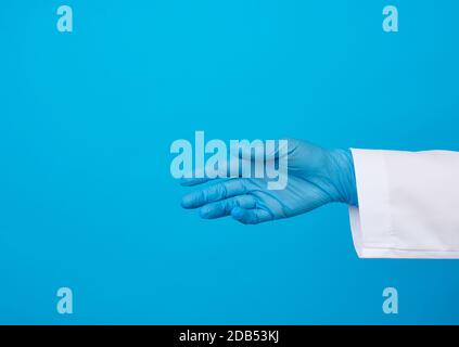 medic in un cappotto bianco, guanti blu in lattice tira la mano per una stretta di mano su uno sfondo blu Foto Stock