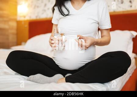 Donna incinta con pancia prende pillole a letto a casa. Gravidanza, calma nel periodo prenatale. Mamma in attesa riposa in camera da letto, stile di vita sano Foto Stock