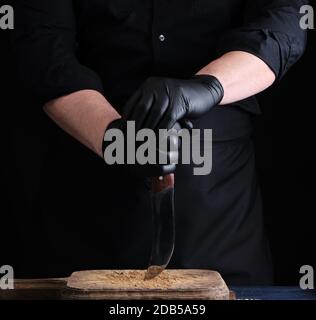 chef in una camicia nera e guanti in lattice nero tiene un coltello da cucina vintage per il taglio della carne, low key Foto Stock