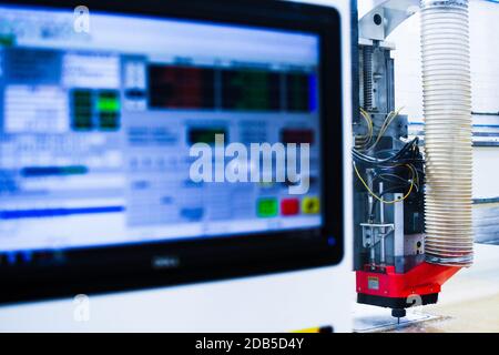 Macchina CNC in plastica ad alta velocità raffigurata con lo schermo del computer in primo piano mentre si taglia una forma di plastica in una fabbrica. Foto Stock