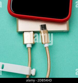 lo smartphone rosso con uno schermo nero vuoto è collegato tramite cavo a un power bank, sfondo verde, vista dall'alto Foto Stock