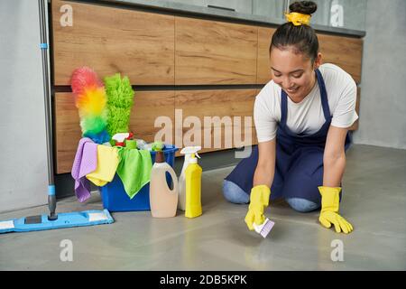 Rendere l'aspetto domestico migliore. Giovane donna allegra che pulisce il pavimento con i detersivi a casa. Lavori di pulizia e pulizia delle camere, concetto di servizio di pulizia Foto Stock