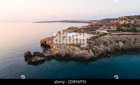 Vista aerea del tramonto della costa e simbolo bianco cappella Agioi Anargyroi, a cavo Greco Protaras, Famagosta, Cipro dall'alto. Vie dell'occhio dell'uccello Foto Stock