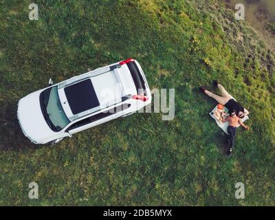 vista dall'alto dell'auto suv e della coppia che si stendono su una coperta sulla spiaggia del fiume Foto Stock