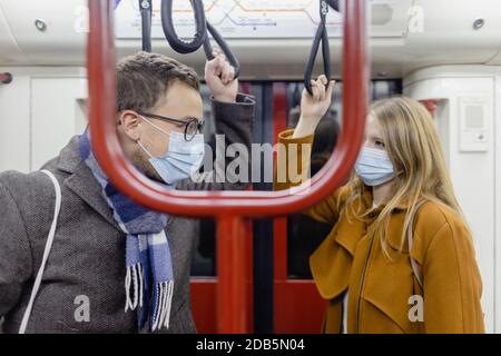 Coppia flirty con covid 19 maschere di faccia in un treno Foto Stock