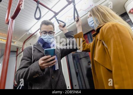 Persone che usano il telefono in treno indossando maschera covid-19 Foto Stock
