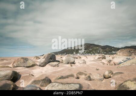 Riprese ad angolo basso attraverso le rocce costiere e la sabbia che guardano verso Barmouth Bay nel Galles del Nord, Regno Unito Foto Stock