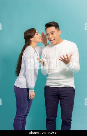 Ritratto di una giovane coppia felice che si erge insieme su sfondo blu, raccontando segreti Foto Stock