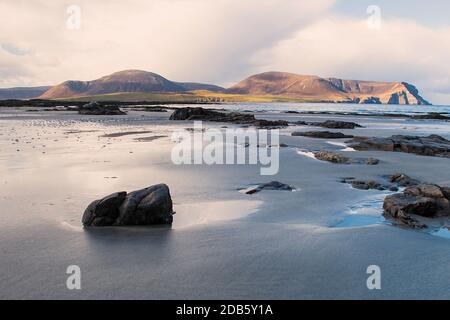 Vista sulla bassa marea della spiaggia sabbiosa con rocce e colline Foto Stock