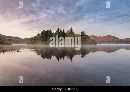 Bella calma riflessioni in un lago nebby in una mattina d'autunno a Derwentwater nel Distretto dei Laghi Inglese. Foto Stock