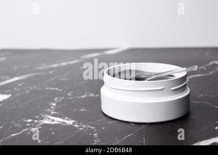 Un vasetto bianco con macchie per gli occhi e spatola sul tavolo in marmo con spazio per la copia. Foto Stock