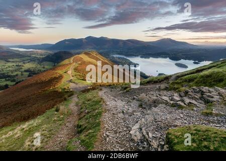 Sentiero roccioso sulle Catbells in autunno mattina con luce solare che colpisce la montagna e l'alba vibrante. Foto Stock