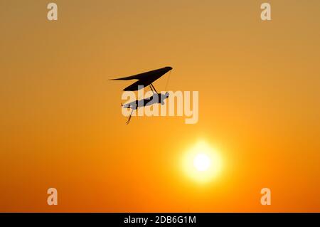 La silhouette dell'ala deltaplano si appende al sole brillante del tramonto. Sogno di volare come un uccello Foto Stock