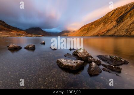 Gruppo di rocce sulla costa del lago Wastwater del Distretto dei Laghi Inglese con drammatiche luci invernali serali e nuvole di luna. Foto Stock