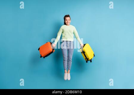 Foto a lunghezza intera del corpo di salto ragazza che mantiene colorato valigie prima del volo in aeroporto isolate su un colore blu brillante sfondo Foto Stock