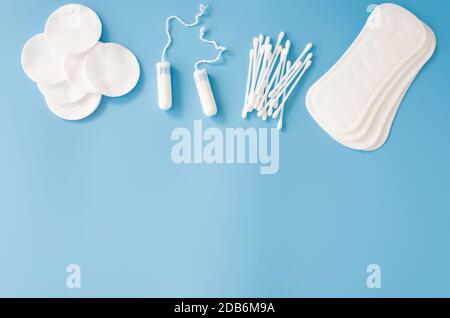 Accessori per l'igiene femminile. Concetto di igiene femminile durante le mestruazioni. Assorbente igienico, tamponi, bastoncini di cotone e batuffoli di cotone su sfondo blu. Foto Stock